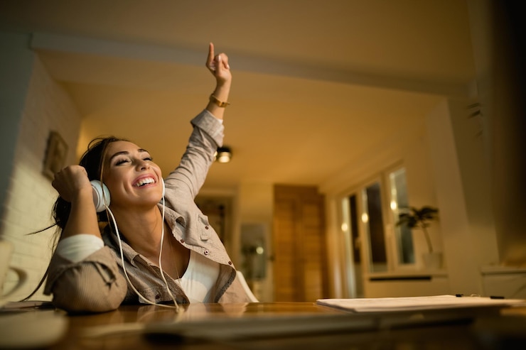 Foto grátis vista de ângulo baixo de mulher feliz se divertindo enquanto ouve música em fones de ouvido à noite em casa