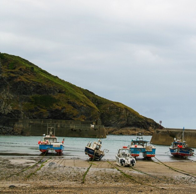 Vista de barcos em uma praia arenosa com uma montanha e um céu nublado