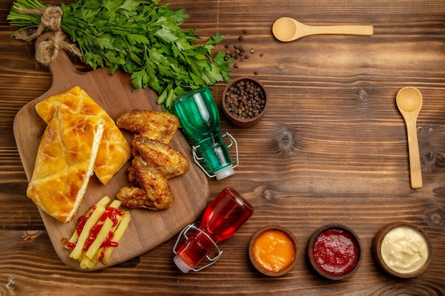 Vista de cima à distância, ervas fastfood, batatas fritas apetitosas, frango e torta no quadro ao lado das colheres de especiarias, frascos e ervas