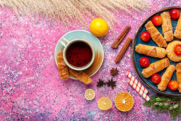 Vista de cima, bagels deliciosos e doces dentro da bandeja com ameixas azedas e chá na superfície rosa claro