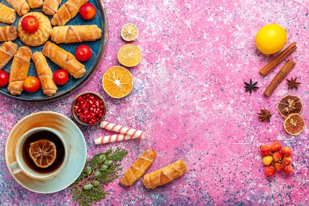 Vista de cima, bagels deliciosos e doces dentro da bandeja com ameixas e xícara de chá na mesa rosa claro