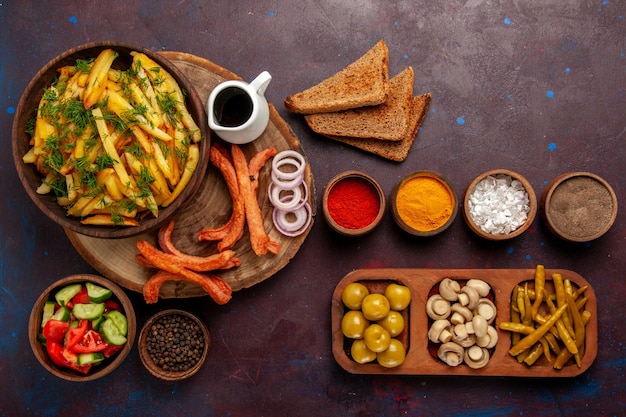 Vista de cima batatas fritas com temperos, pães e vegetais diferentes na mesa escura