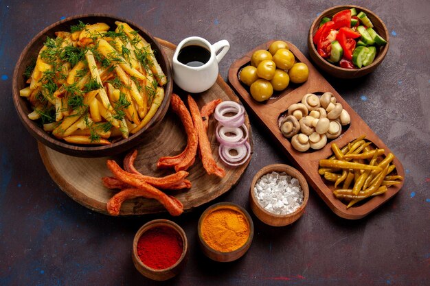 Vista de cima batatas fritas saborosas batatas fritas com salsichas e temperos diferentes na mesa escura