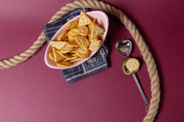 Vista de cima biscoitos salgados dentro de um prato rosa com cordas no fundo rosa, biscoito crocante lanche cor de comida