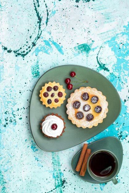 Vista de cima bolinhos com chá e canela na mesa azul claro torta de bolo doce de cereja