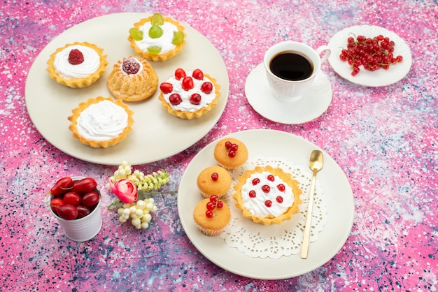 Vista de cima bolinhos com creme de frutas frescas e uma xícara de café dentro de um prato branco na mesa iluminada