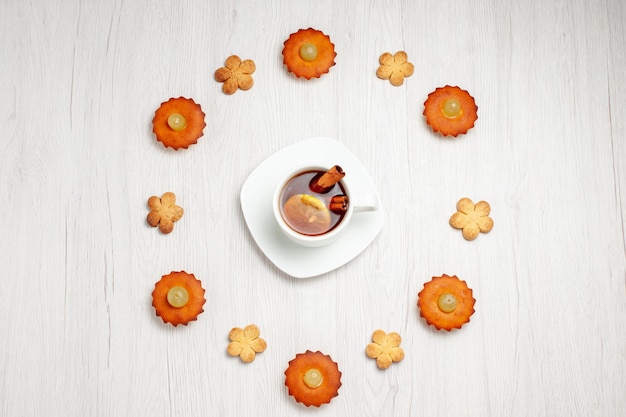 Vista de cima bolinhos deliciosos forrados com biscoitos e uma xícara de chá na superfície branca