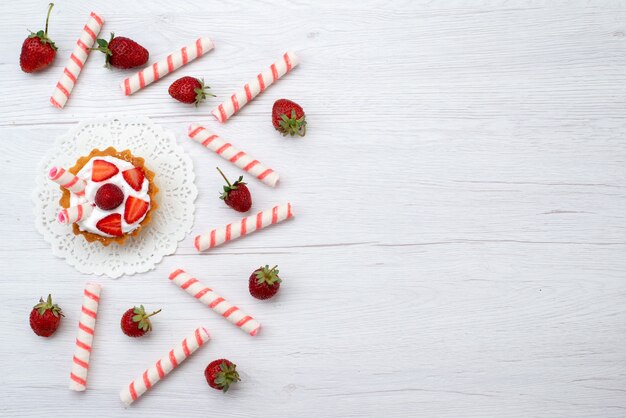 Vista de cima bolinhos gostosos com creme e morangos fatiados no fundo branco bolo baga doce assar