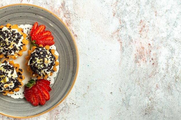 Vista de cima bolinhos gostosos com creme e morangos na superfície branca Bolo de festa de aniversário biscoito doce