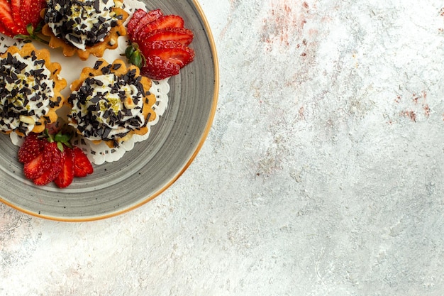 Vista de cima bolinhos saborosos com creme e morangos em uma superfície branca clara bolo de festa de aniversário biscoito doce