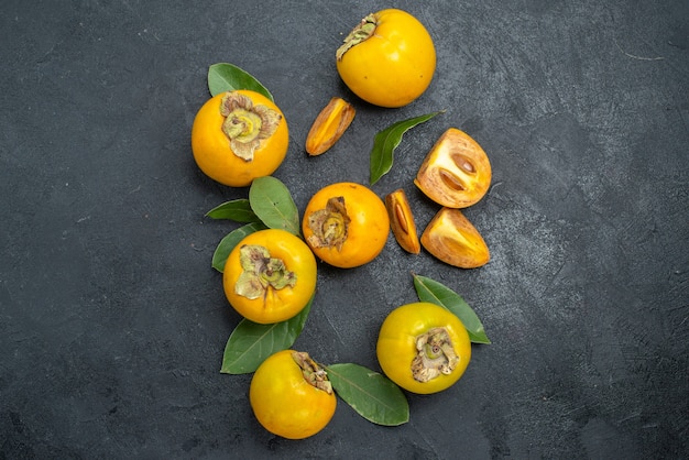 Vista de cima caquis doce com folhas na mesa escura com gosto de frutas maduras