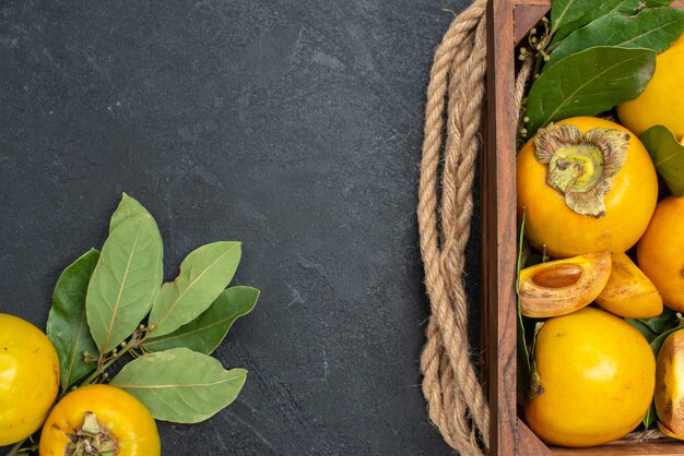 Vista de cima caquis doces frescos dentro de uma caixa em piso escuro com sabor de frutas maduras