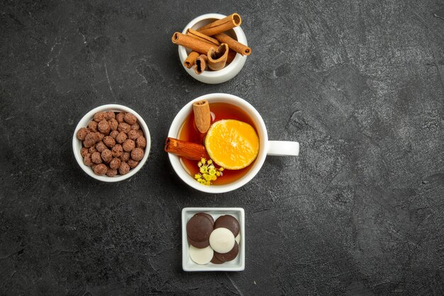 Vista de cima com chocolate e nozes, tigelas com bastões de cinnabon, chocolate e nozes e uma xícara de chá com cinnabon e limão no lado esquerdo da mesa