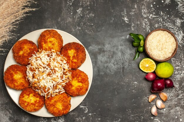 Vista de cima costeletas fritas com arroz cozido em um prato de comida de superfície escura rissole de carne