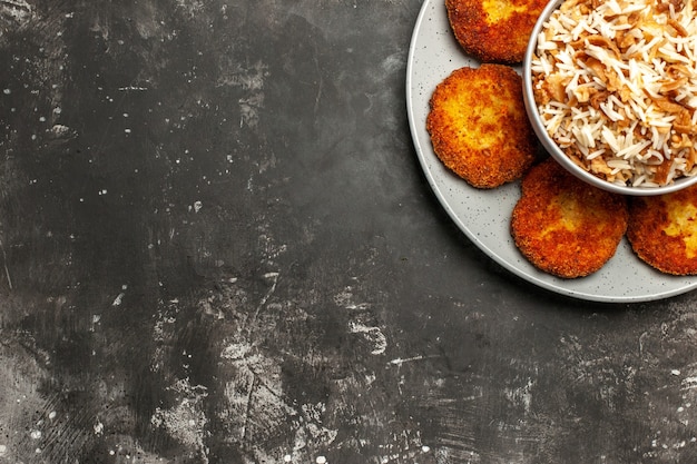 Vista de cima costeletas fritas com arroz cozido em um prato de superfície escura com carne rissole