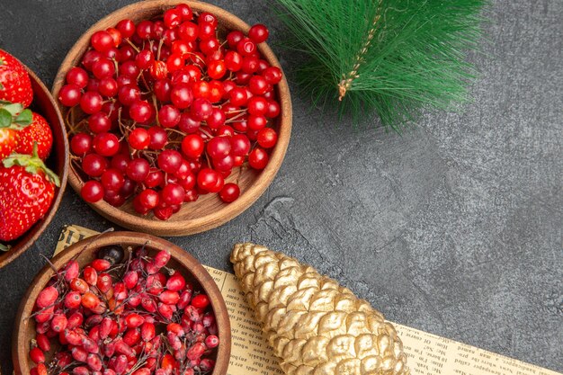 Vista de cima cranberries vermelhos frescos com outras frutas em volta dos brinquedos de Natal em fundo escuro