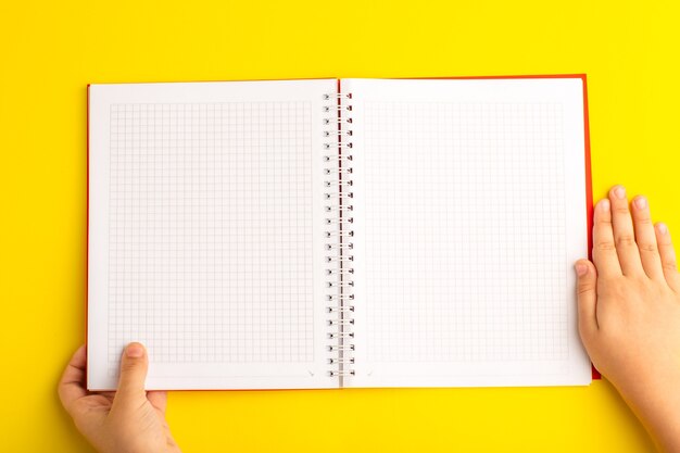 Vista de cima, criança segurando o caderno na mesa amarela