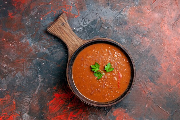 Vista de cima da clássica sopa de tomate em uma tábua de corte marrom em uma mesa de cores misturadas