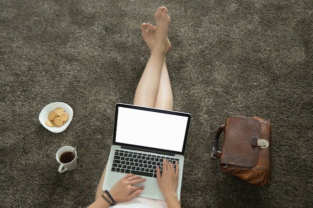 Vista de cima da mulher deitada no tapete com um laptop