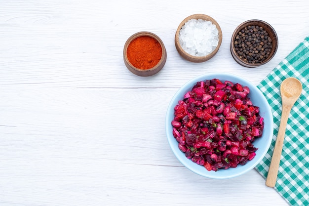 vista de cima da salada de beterraba fatiada com verduras dentro de um prato azul com temperos na mesa iluminada, salada de alimentação saudável com vitaminas