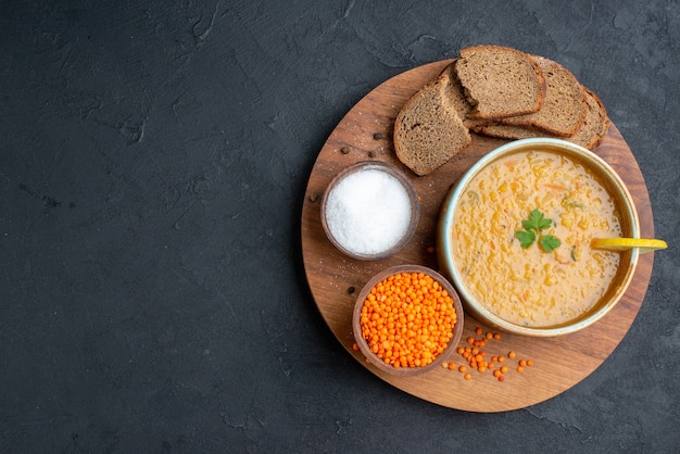 Vista de cima da sopa de lentilhas com lentilhas crus salgadas e pães escuros na superfície escura