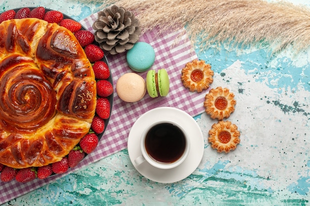 Vista de cima da torta de morango com biscoitos, macarons e uma xícara de chá na superfície azul
