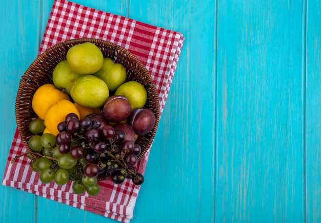 Vista de cima das frutas enquanto as uvas plantam nectacotes na cesta em tecido xadrez e fundo azul com espaço de cópia