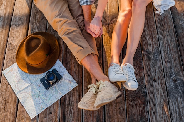 Vista de cima das pernas de um casal viajando no verão vestido com tênis, moda estilo boho hipster de homem e mulher se divertindo juntos, mapa, chapéu, câmera fotográfica, passeios turísticos, moda de calçados