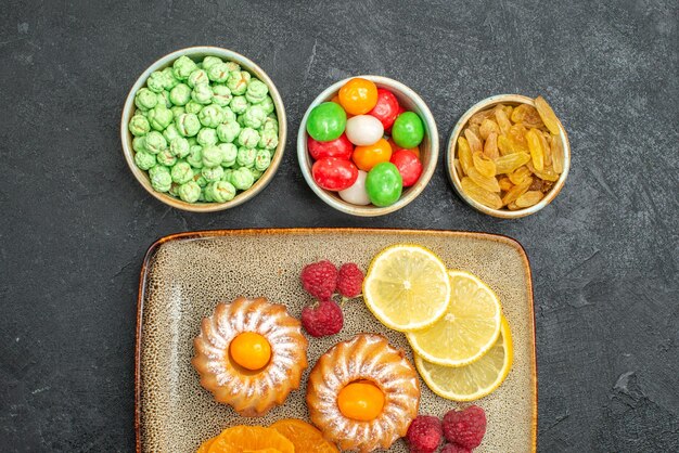 Vista de cima de bolinhos com rodelas de limão, tangerinas e doces em preto