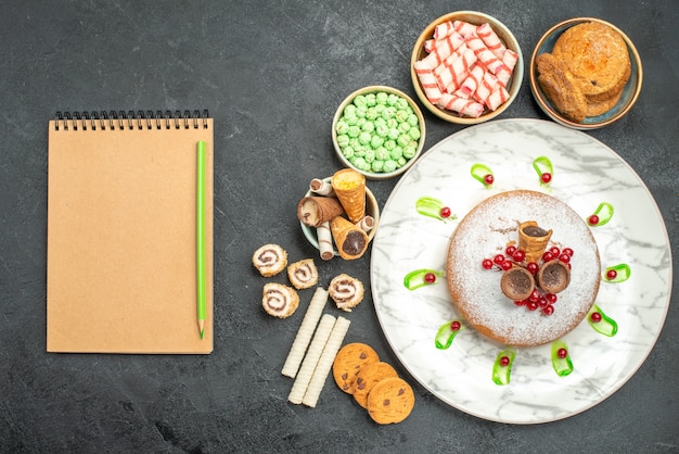 Vista de cima de cima de doces, um bolo com groselha, doces coloridos, waffles, lápis, caderno