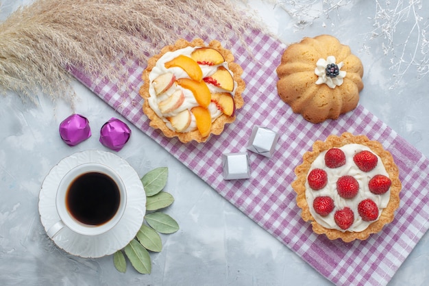 Vista de cima de deliciosos bolos cremosos com frutas fatiadas junto com bombons de chocolate e chá no chão claro bolo biscoito doce creme asse chá açúcar