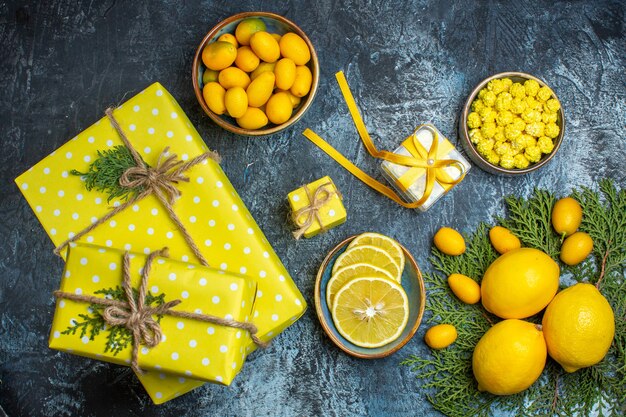 Vista de cima de doces de frutas cítricas frescas inteiras e pela metade em uma panela e caixas de presente amarelas em fundo escuro