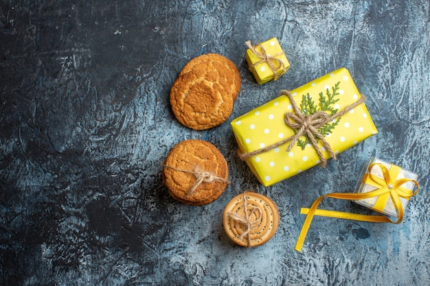 Vista de cima de lindas caixas de presente de natal amarelas empilhadas e vários biscoitos em fundo escuro