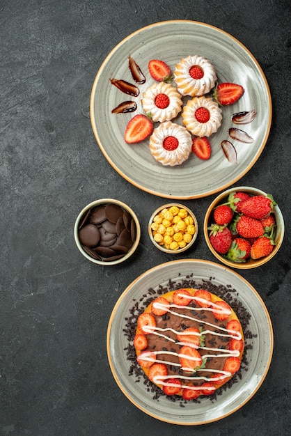 Vista de cima de longe, doces e bolo, biscoitos de morango e bolo com chocolate e tigelas de chocolate de noz de morango no lado direito da mesa preta