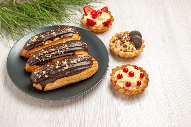 Vista de cima de perto éclairs de chocolate nas tortas de prato cinza e as folhas do pinheiro no lado esquerdo do chão de madeira branco