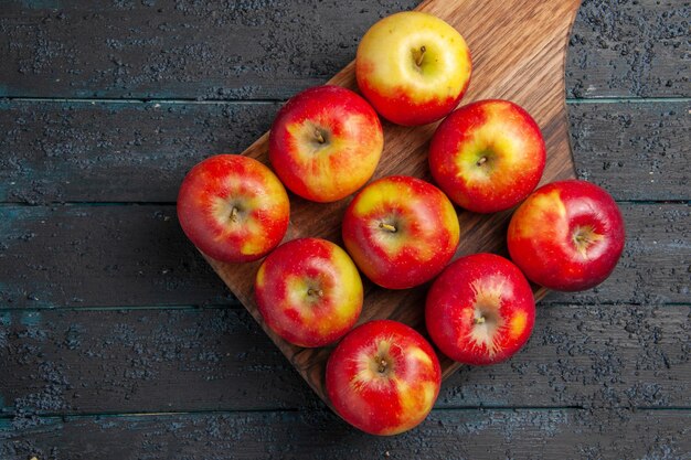 Vista de cima de perto maçãs a bordo de nove maçãs amarelo-vermelhas em uma tábua de madeira na mesa cinza