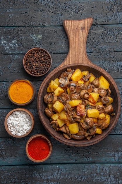 Vista de cima de perto o prato de comida e temperos um prato de cogumelos e batatas na tábua e diferentes temperos ao redor