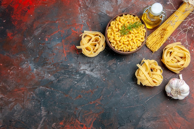 Vista de cima de três porções de espaguete e macarrão com borboletas em uma tigela marrom e cebola verde e limão com garrafa de óleo de alho e limão na mesa de cores diferentes