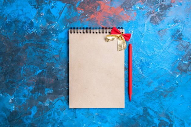 Vista de cima de um bloco de notas com um pequeno laço de lápis vermelho sobre fundo azul com espaço de cópia
