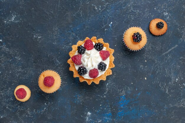 Vista de cima de um delicioso bolo doce com diferentes frutas e creme saboroso em uma mesa cinza-escuro, doce de biscoito de bolo de cor de frutas silvestres