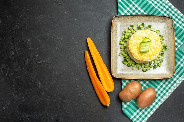 Foto grátis vista de cima de uma deliciosa salada servida com pepino picado em uma toalha verde despojada pela metade e batatas com cenoura em fundo escuro