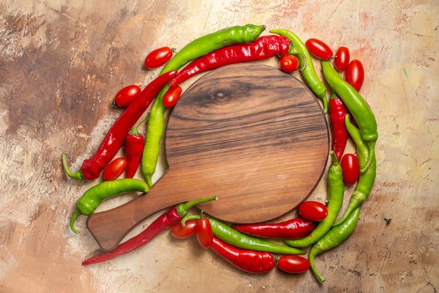 Foto grátis vista de cima de uma tábua de cortar cercada por pimentas e tomates cereja em fundo âmbar