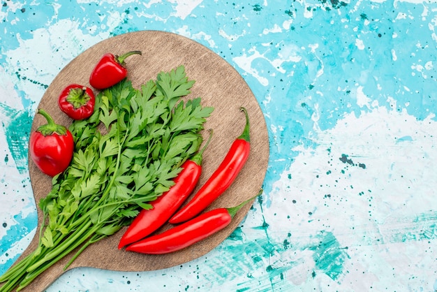 Vista de cima de verduras frescas junto com pimentas vermelhas picantes no ingrediente alimentar verde vegetal, azul brilhante