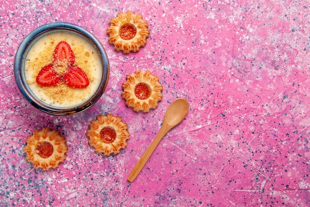 Vista de cima deliciosa sobremesa cremosa com morangos fatiados em fatias vermelhas e biscoitos no fundo rosa.