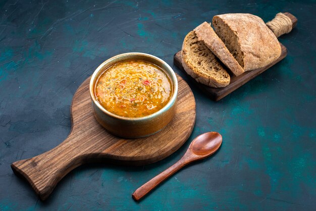 Vista de cima, deliciosa sopa de vegetais dentro de prato redondo com pão na mesa azul escura.