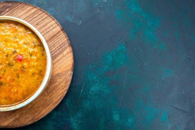 Vista de cima deliciosa sopa de vegetais dentro de prato redondo na mesa azul escura.