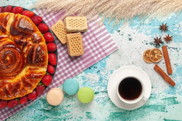 Vista de cima deliciosa torta com morangos vermelhos, macarons franceses e waffles na superfície azul