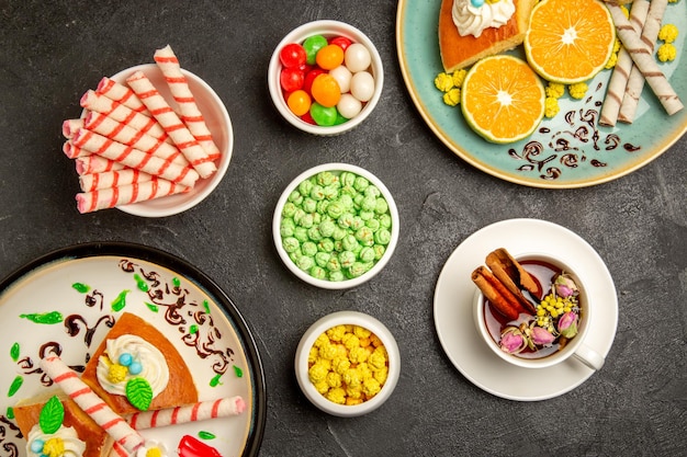 Vista de cima deliciosas fatias de torta com tangerinas fatiadas sobre fundo cinza escuro frutas doces bolo massa de torta chá