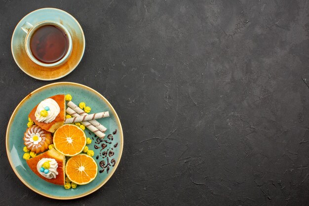 Vista de cima deliciosas fatias de torta com tangerinas frescas e uma xícara de chá no escuro