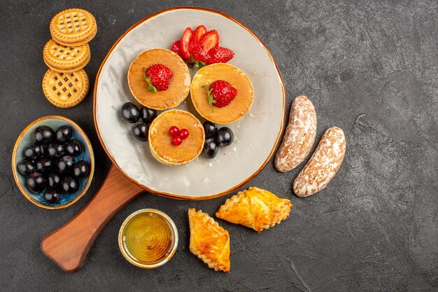 Vista de cima deliciosas panquecas com frutas e bolos no escuro